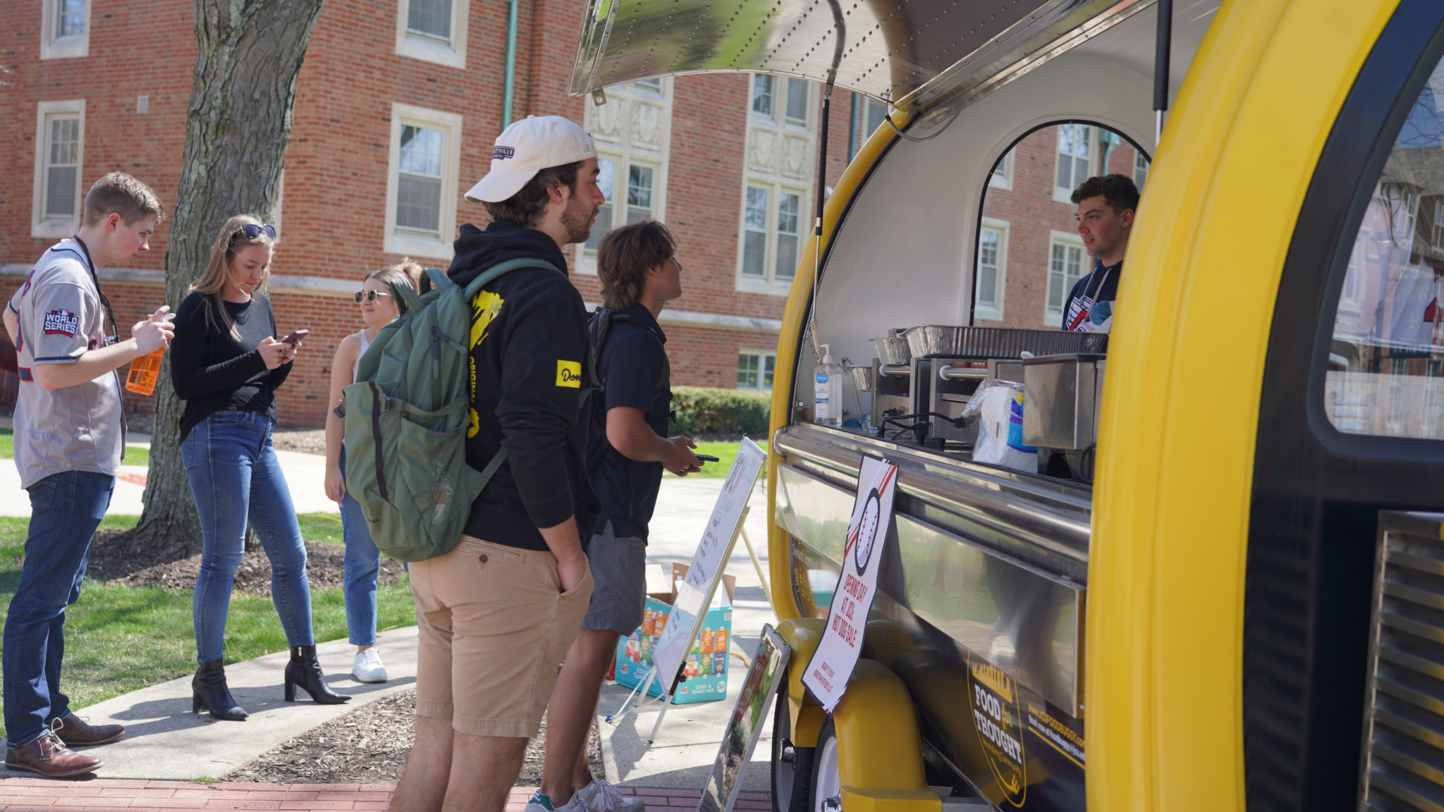 Multiple students waiting in line to order food from a small yellow and blue cart.